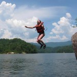 Cmapers jumping off rock into the lake